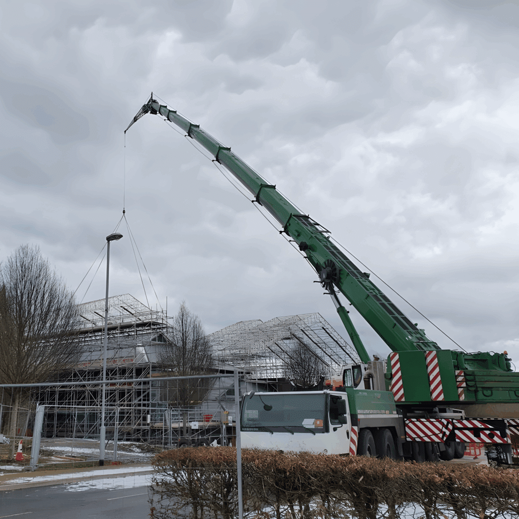 Liebherr all-terrain crane rigged with a long main boom beside the scaffolded building