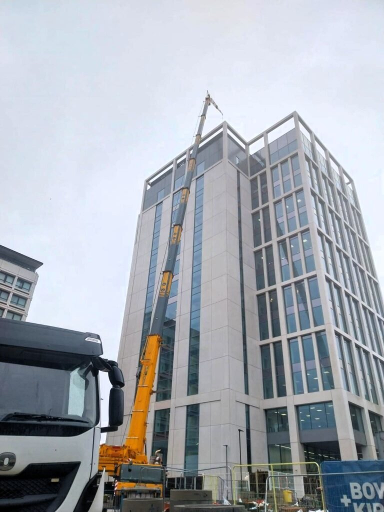 Mobile crane with fly jib rigged beside a 64m building, with transport alongside