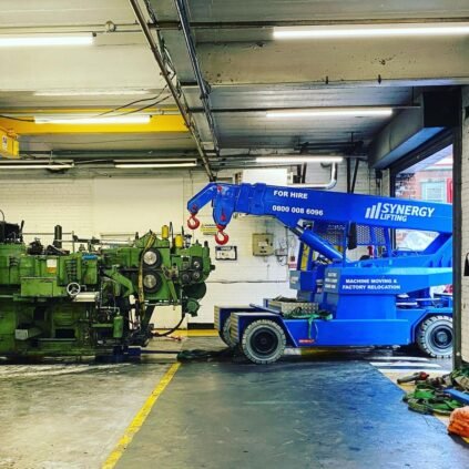A blue electric pick and carry crane beside a large green machine inside a factory unit