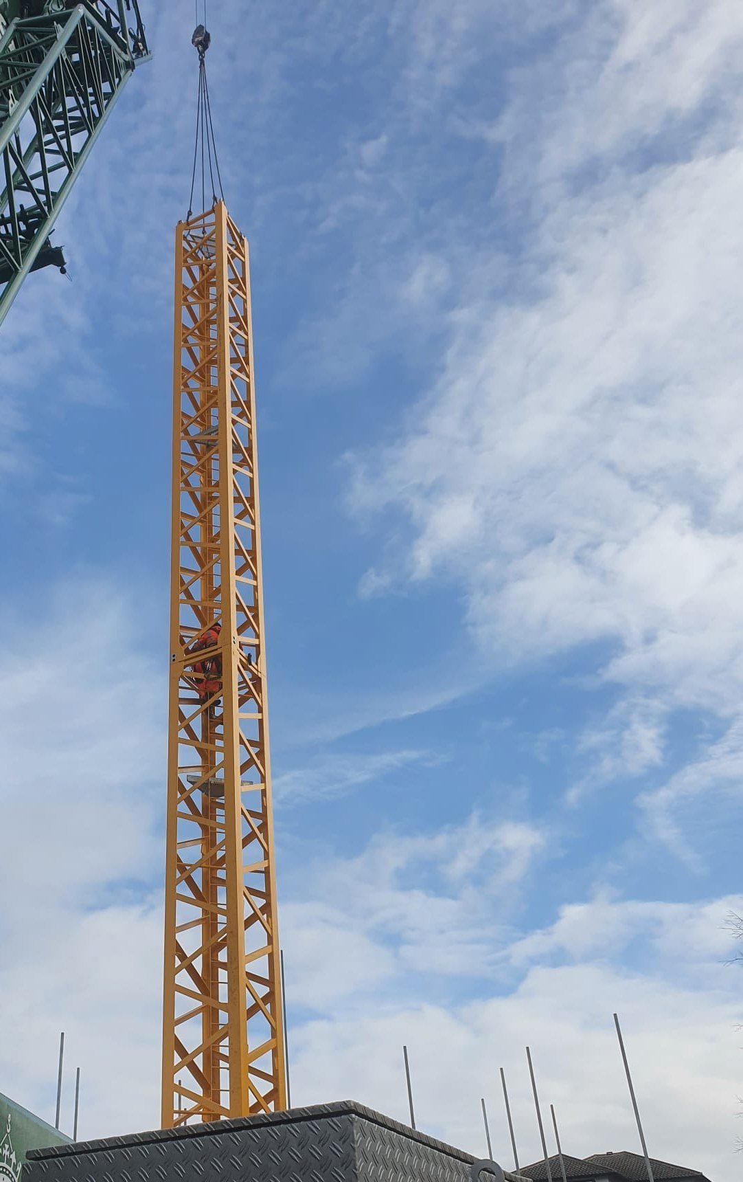 A mast section hanging from the erection crane during the tower crane erection at Lampton Road, Hounslow, with a rigger working on the mast