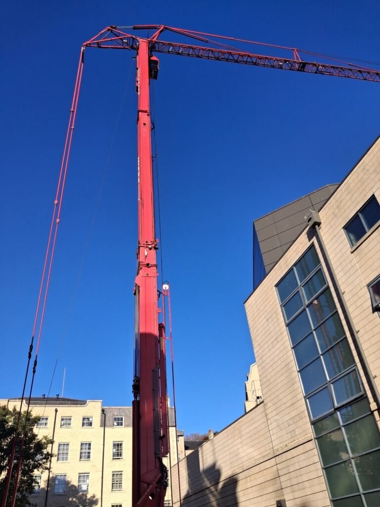 Mobile tower crane with its tower raised and jib reaching over the roof of a leisure complex in Bath for a chiller lift
