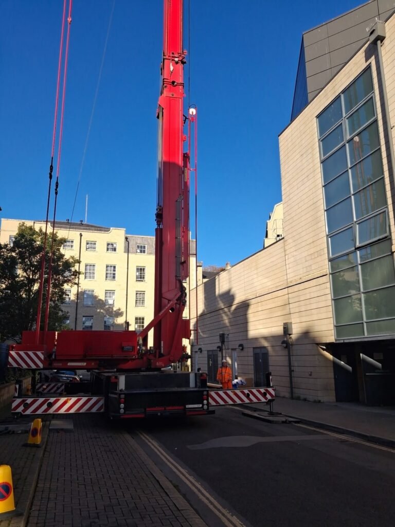 Mobile tower crane rigged on outrigger mats beside a leisure complex in Bath, with the road closed to traffic