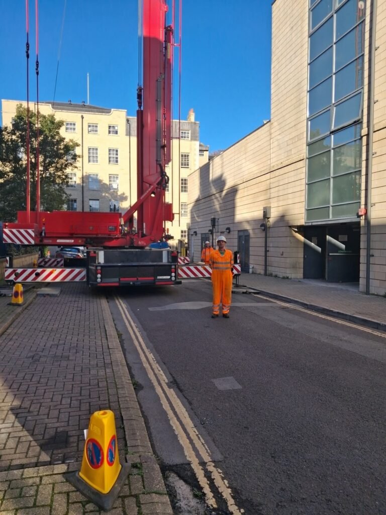 Mobile tower crane on outriggers on a narrow street in Bath city centre, with the road closed and a lift supervisor standing by