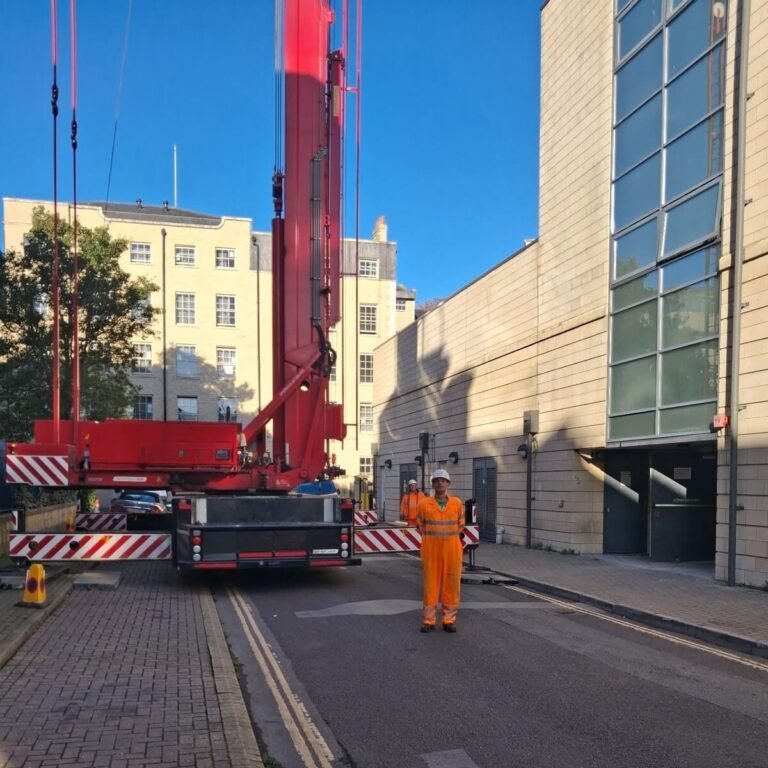 Mobile tower crane on outriggers on a closed street in Bath, behind Chapter 8 barriers, with a lift supervisor standing by