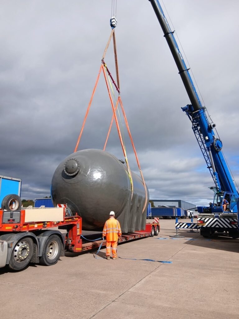 Filter vessel being lowered onto a low loader in the West Midlands by a 60te all-terrain crane, rigged with a spreader beam and cradle slings